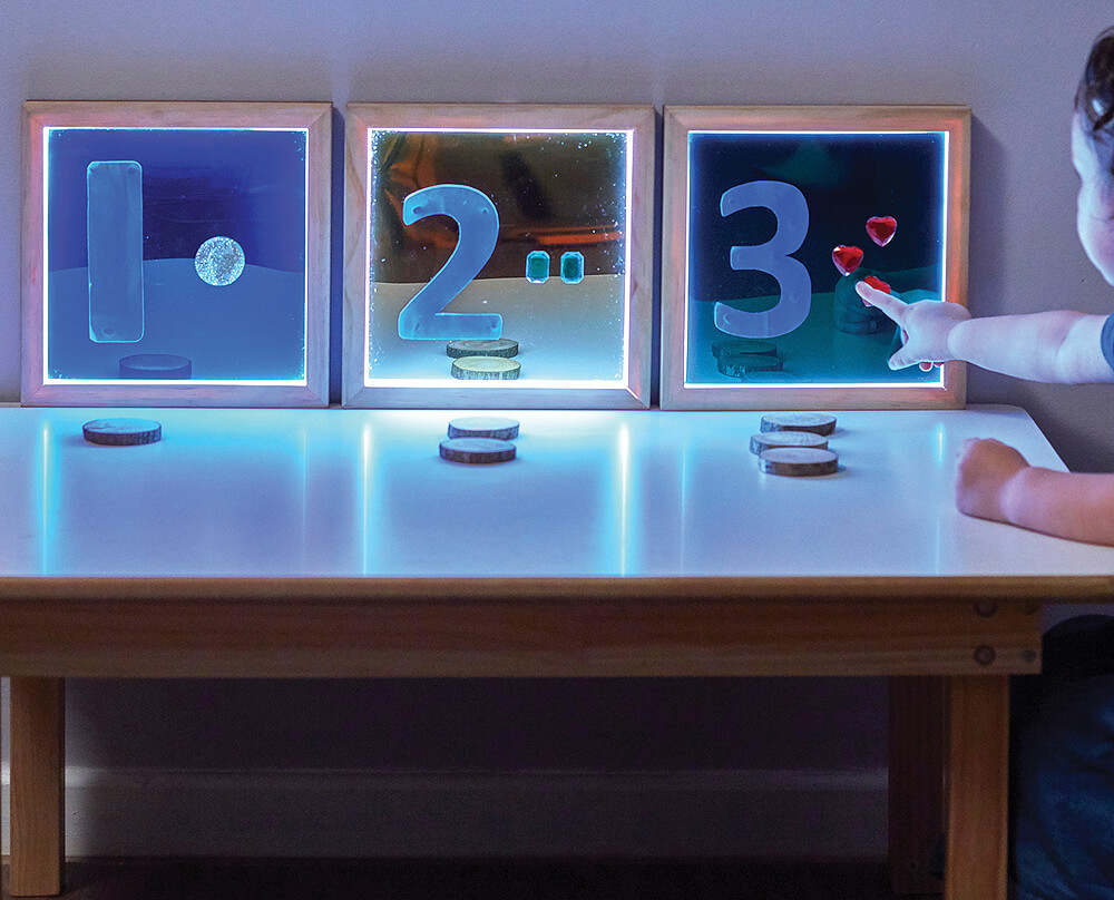 Dítě se učí počítat pomocí svítících číselných tabulek a přírodních žetonů během interaktivní činnosti.