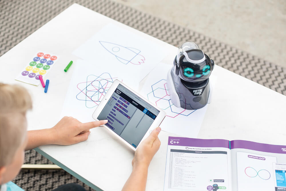 Dítě programuje interaktivního robota pomocí tabletu a učebnice během edukační aktivity.